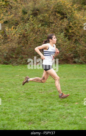 Bruna giovane lady runner rivestito in pioggia e fango affacciate agli elementi nel cross country race con silenziatore campo di erba al calpestio Foto Stock