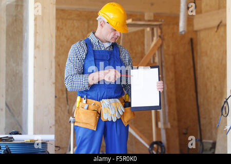 Costruzione foreman indossando un giallo casco di sicurezza tenendo un clipboard Foto Stock
