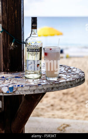 Una bottiglia di Cruzan Rum invecchiato e un cocktail di rum in un bicchiere, il mare dei Caraibi in background. Foto Stock