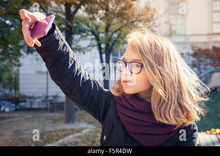 Bella bionda caucasica ragazza adolescente prendendo foto sul suo smartphone nel parco autunnali Foto Stock