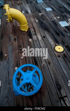 Una valvola blu e una tubazione gialla sul ponte di una nave da battaglia. Foto Stock