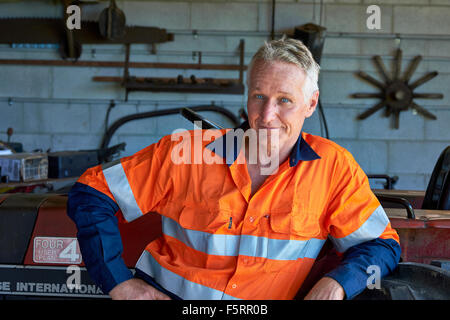 Ritratto di un agricoltore nei panni di sicurezza accanto al suo trattore Foto Stock