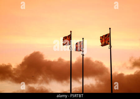 3 unione jack bandiere in un vento forte contro un orange sunrise sky Foto Stock