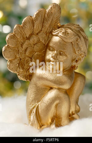 Golden Angel figura sulla soffice materiale bianco, con luci sfocate in background Foto Stock