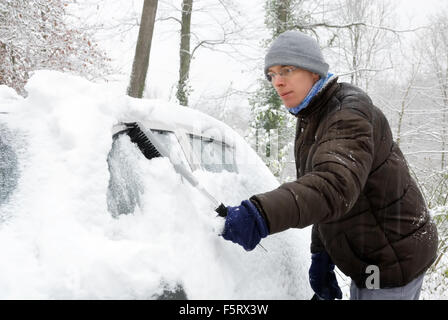 Giovane uomo spazzolando la neve fuori la sua auto in una fredda giornata invernale Foto Stock