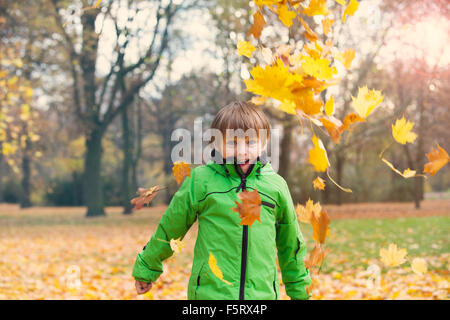 Ragazzo in park in autunno a giocare con foglie Foto Stock