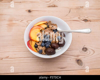 Una ciotola di cereali per la prima colazione di fiocchi di crusca con mirtilli prugne e pesche noci fette Foto Stock