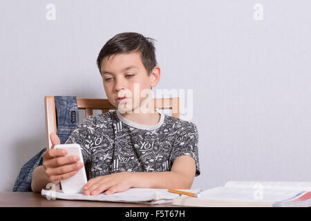 Pre-teen boy distratto dal suo telefono di svolgere i suoi compiti Foto Stock