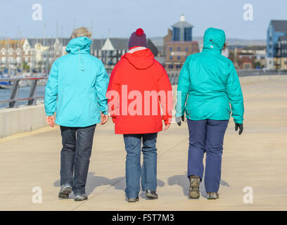 3 women wearing coats, walking away on a cold damp day in Winter in West Sussex, England, UK. Foto Stock