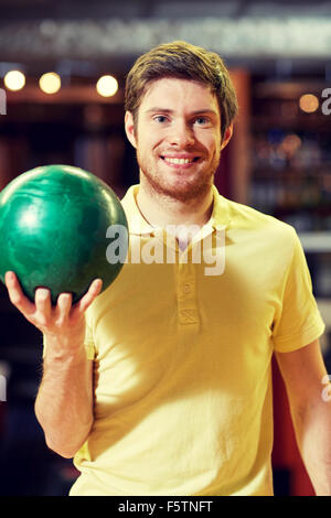 Felice giovane tenendo palla in bowling club Foto Stock