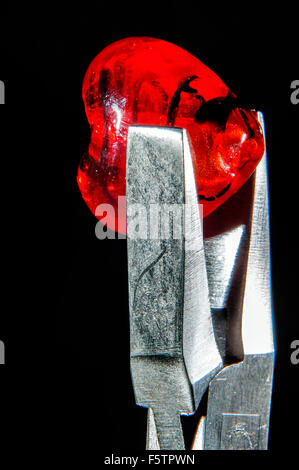 Da gioielliere pinze tenendo cuore rosso a forma di cordone di vetro in studio di impostazione Foto Stock