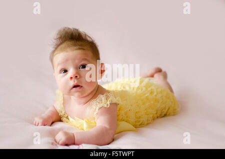 Bellissima bambina giacente sulla pancia che indossa abiti di colore giallo Foto Stock