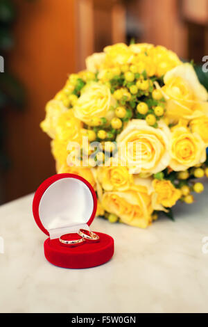 Gli anelli di nozze nella custodia rossa su uno sfondo di colore giallo sposa bouquet Foto Stock