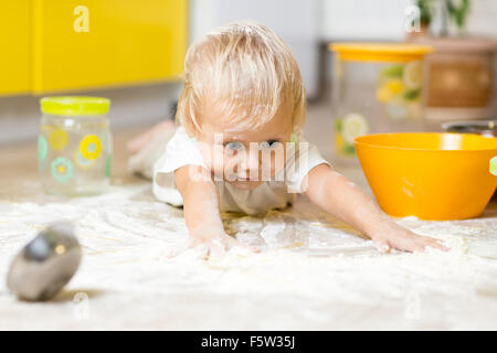 Bambino posa su disordinatissimi cucina, pavimento ricoperto di bianco di farina Foto Stock