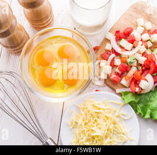 La frittata ingredienti: uova fresche verdure tagliate, il latte e il formaggio sul tavolo di legno. Foto Stock
