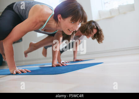 Due donne a yoga classe facendo yoga stand mano posa. Donna matura in piedi sulle mani con i piedi sollevati facendo yoga gru pongono - B Foto Stock