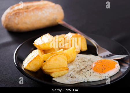 La prima colazione con patate fritte e uova su una piastra scuro Foto Stock