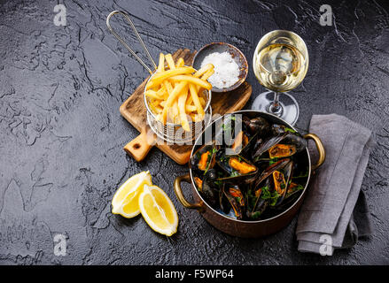 Le cozze in rame piatto di cottura con il vino e le patatine fritte in pietra nera sullo sfondo Foto Stock