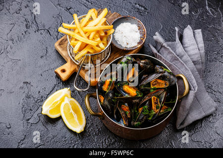 Le cozze in rame piatto di cottura e patatine fritte sulla pietra nera sullo sfondo Foto Stock