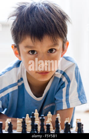 Bambino caucasico, 7 anni, boy, giocare a scacchi di gioco. Dritto in Visualizza come egli guarda oltre i pezzi di scacchi e sorrisi al visualizzatore. Fiducioso di espressione. Foto Stock