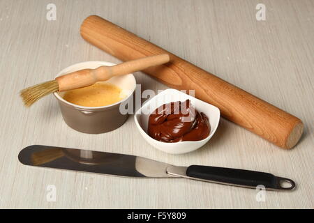 Perno di rotolamento, coltello tavolozza, cioccolato, uovo smalto, spazzola. Fare croissant al cioccolato con pasta sfoglia Foto Stock