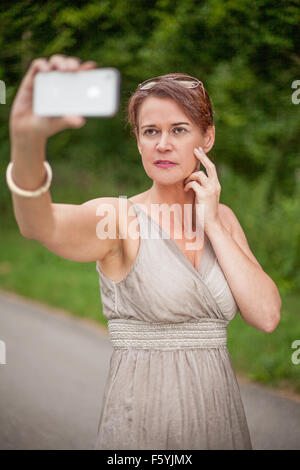 La donna in vestaglia tenendo Autoritratto con un telefono cellulare Foto Stock