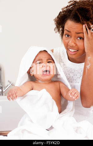 Giovane madre con il suo figlio di pianto dopo la sua vasca da bagno. Sta cercando un computer ha sottolineato con la sua mano sulla testa Foto Stock