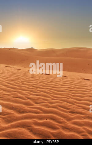 Il paesaggio del deserto , il tramonto dietro le dune di sabbia, persone sagome in background e orme nella sabbia Foto Stock