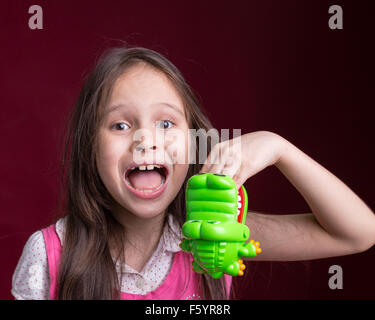 Giovani asiatici ragazza americana con coccodrillo verde toy mordere la mano Foto Stock