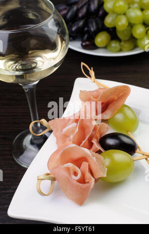 Antipasto di prosciutto e Uva su uno spiedino con un bicchiere di vino bianco Foto Stock