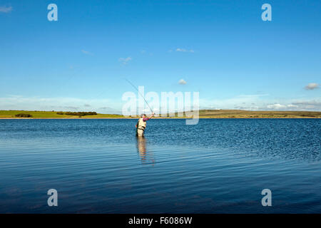 La pesca a mosca sul serbatoio Colliford lago Bodmin Moor Cornwall lone uomo casting con asta sul lago ancora cielo blu Foto Stock