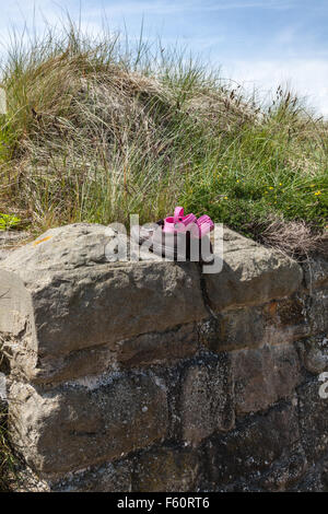 Un bambino scarpe rosa nascosto in una coppia di formatori dalla parete del porto a Seaton Sluice, Tyne and Wear, England, Regno Unito Foto Stock