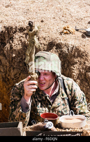 La seconda guerra mondiale la rievocazione. Vista guardando verso il basso in corrispondenza ufficiale tedesco che indossa il camuffamento smock, stando in trincea guardando attraverso il periscopio. Foto Stock