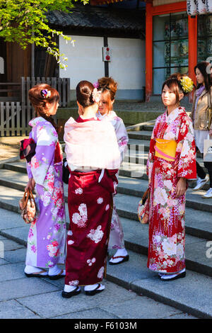 Quattro giovani donne giapponesi che indossa kinomo chat permanente per ogni altro sui gradini della porta d'ingresso al santuario Yasaka a Kyoto in primavera. Foto Stock