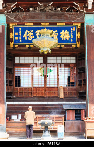 Giappone, Kyoto, Seiryo-ji. Distante shot. Vista da dietro del senior uomo in piedi di fronte a temple hall pregando accanto al fumo di incenso bruciatore. Foto Stock