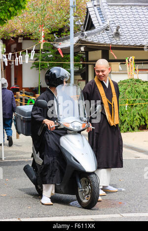 Giappone, Nishinomiya, Mondo Yakuji, Shotaizan Tokoji tempio, prete buddista nelle vesti su scooter a parlare con un altro monaco in piedi accanto a lui. Foto Stock