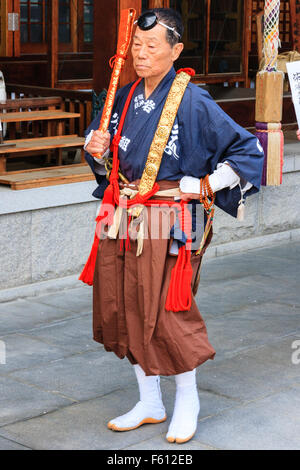 Giappone, Nishinomiya, Tokoji Shotaizan tempio. Sacerdote di monaco guerriero costume, Yamabushi, tunica blu, marrone pantaloni, in piedi fuori aula del tempio. Foto Stock