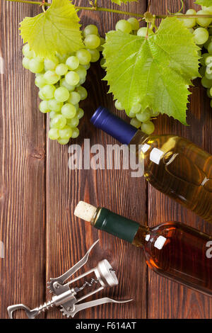 Grappolo di uva, vino bianco bottiglie e cavatappi sul tavolo di legno Foto Stock