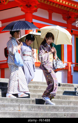 Giappone, Kyoto, tre donne che indossano il kimono e azienda tende da sole Ombrelloni, attentamente a piedi giù per la scalinata in pietra all'ingresso del santuario Yasaka. Foto Stock