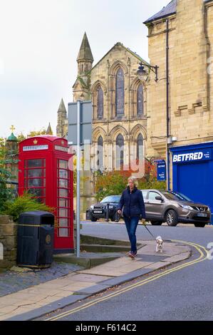 La donna a piedi passato cane rosso nella casella Telefono. Hexham Abbey in background. Hexham, Northumberland, Inghilterra, Regno Unito. Foto Stock