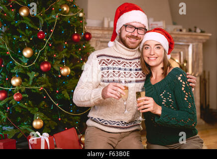 Coppia felice in Santa caps scanalature di contenimento con champagne da albero di Natale Foto Stock