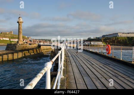 Estiva soleggiata vista serale di persone rilassante sul molo Ovest, Whitby, North Yorkshire, GB - scenic town, faro e ingresso del porto, al di là. Foto Stock