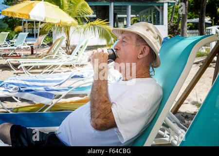 77 anni uomo caucasico bevande un soft drink durante i momenti di relax sulla spiaggia di St. Croix, U.S. Isole Vergini. Foto Stock