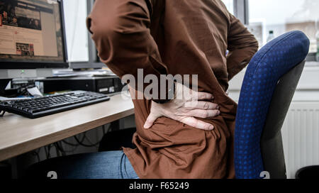 Illustrazione: Un dipendente si siede alla sua scrivania in ufficio e mantiene il suo male torna a Dresda (Sassonia), Germania, 04 febbraio 2015. Foto: Thomas Eisenhuth/dpa Foto Stock