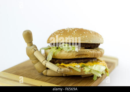 Il burattino di legno in piedi su un tagliere contro uno sfondo bianco, tenendo un hamburger Foto Stock