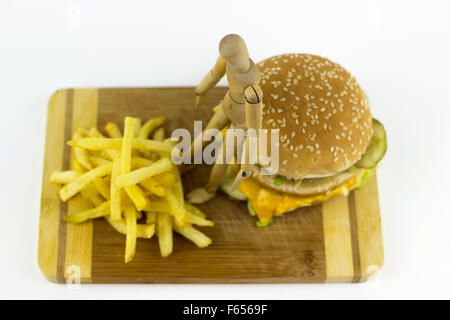 Il burattino di legno in piedi su un hamburger, guardando alcune patate fritte Foto Stock