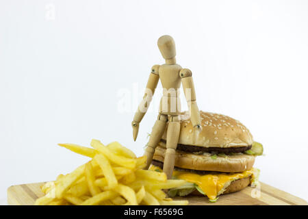 Il burattino di legno in piedi su un hamburger, guardando alcune patate fritte Foto Stock