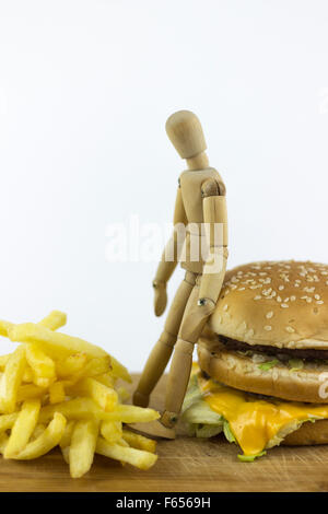 Il burattino di legno in piedi su un hamburger, guardando alcune patate fritte Foto Stock