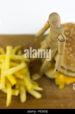 Il burattino di legno in piedi su un hamburger, guardando alcune patate fritte Foto Stock