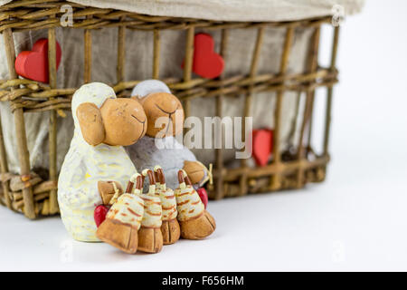 Due pecore figurine davanti a un vintage rattan cestello, su sfondo bianco Foto Stock